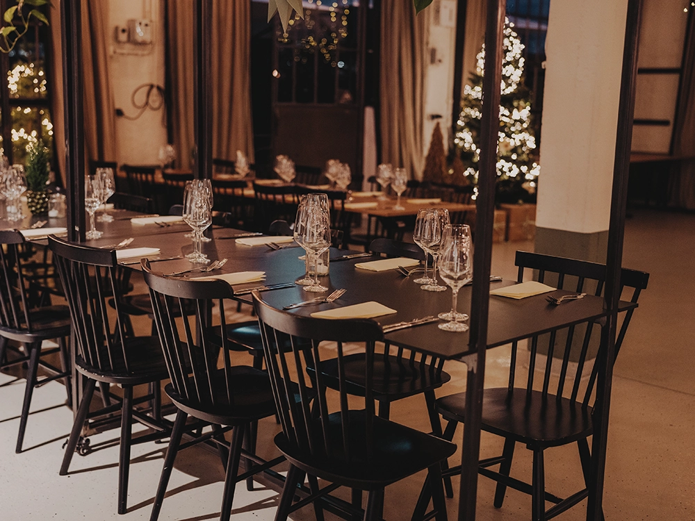 Eleganter Speisesaal mit gedeckten Tischen, leeren Gläsern und Weihnachtsbaum im Hintergrund, warm beleuchtet.