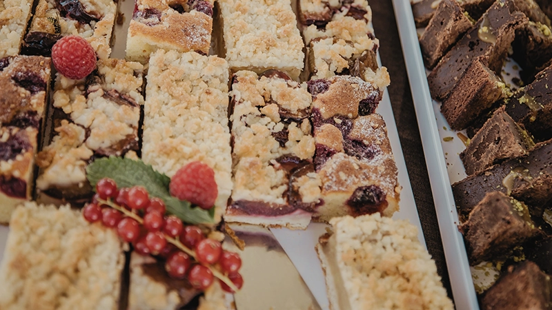 Verschiedene Kuchenstücke auf einem Tablett, darunter Streuselkuchen mit Kirschen und Schokoladenkuchen, dekoriert mit Beeren.