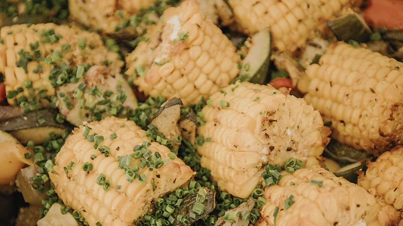 Gebratene Maiskolbenstücke mit gehacktem Schnittlauch, serviert auf einer Gemüsemischung aus Zucchini und Karotten.