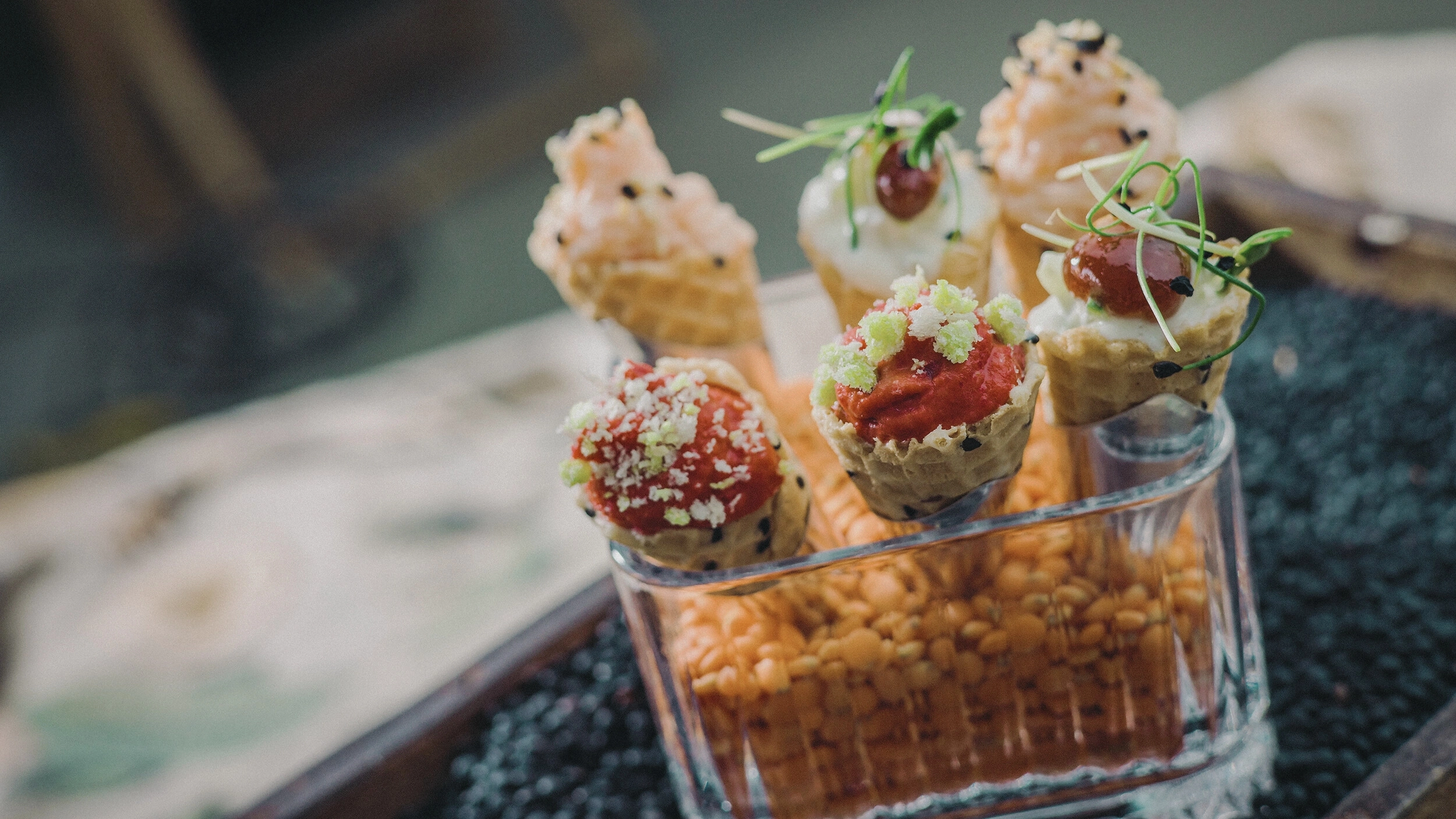 Mini-Waffeltüten mit verschiedenen festlichen Belägen, präsentiert in einem Glasbehälter auf Linsen.