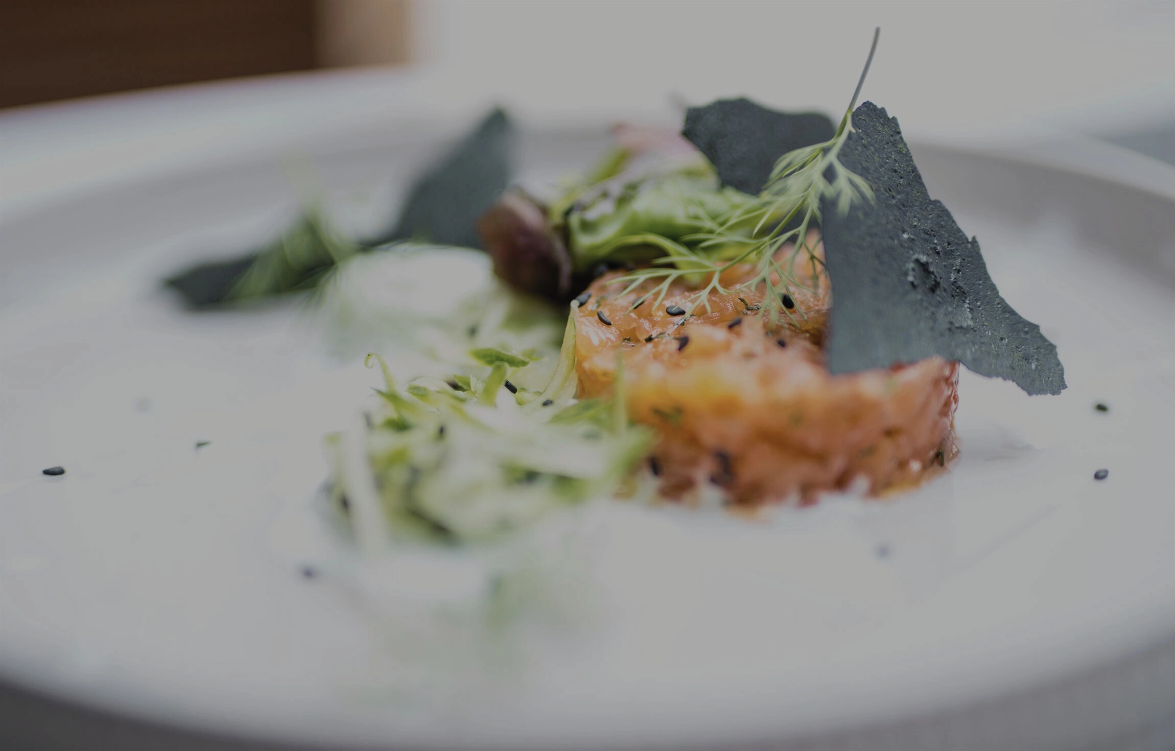 Elegantes Lachstatar mit Dill, Gurke und schwarzem Sesam auf weißem Teller angerichtet.