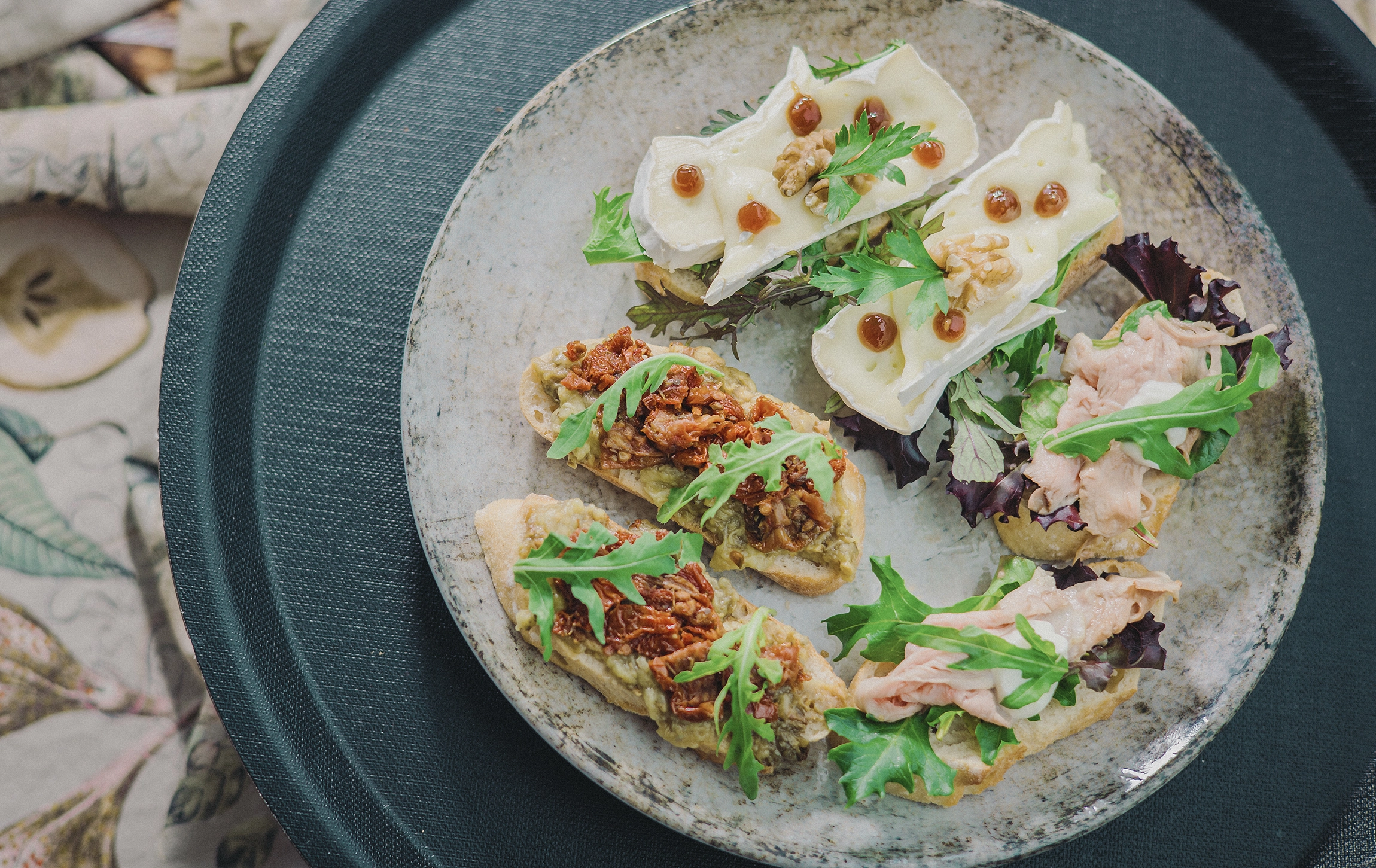 Verschiedene Canapés auf einem Teller, belegt mit Käse, Nüssen, Salat, Avocado und Aufschnitt, auf einem Tisch serviert.
