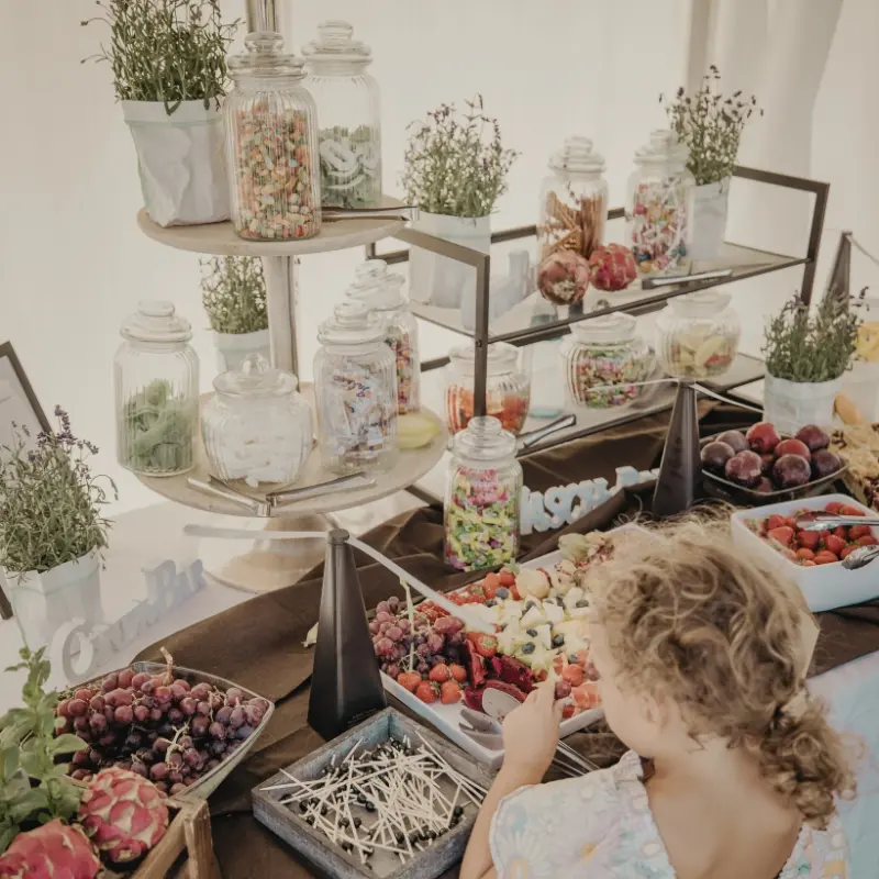 3_1 Kind vor Süßigkeiten-Tisch mit Glasgefäßen und frischem Obst. Lavendelpflanzen dekorieren die Szene.