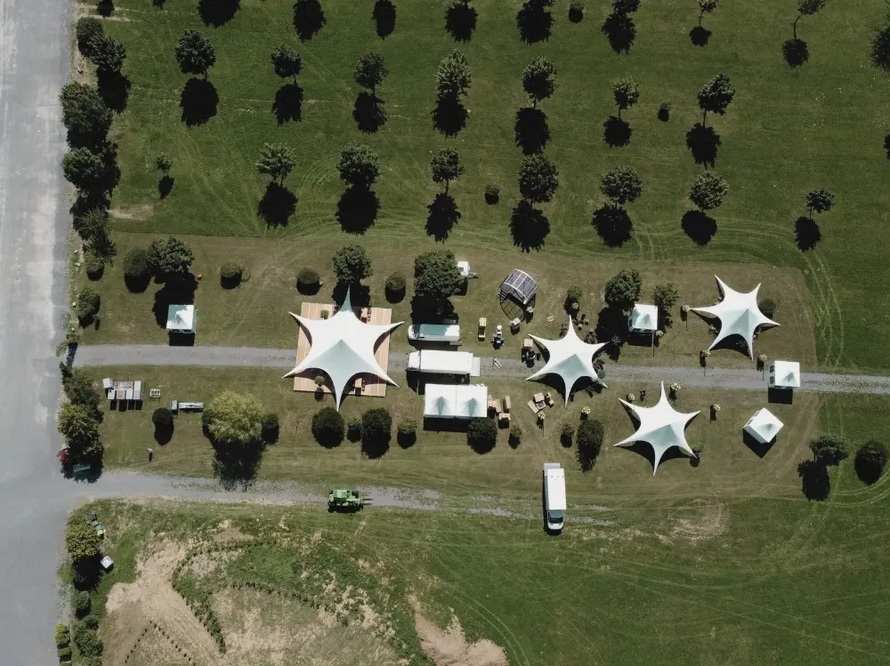 6 Luftaufnahme eines Parks mit weißen Festzelten, umgeben von Bäumen und Fahrzeugen auf Grasflächen.